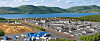 Großes Bauareal mit Gebäuden, Straßen und Materialflächen am See vor Bergen.