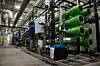 Innenansicht einer Industriehalle mit grünen Rohrleitungen und technischen Anlagen entlang eines Gangs.
