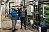 Zwei Männer in einer Industriehalle neben Rohrleitungen und Anlagen der Wasseraufbereitung.