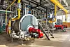 Industriekesselraum mit drei großen Kesseln, roten Pumpen und vielen Rohrleitungen.