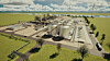 Luftansicht einer Industrieanlage mit großen Tanks, Gebäuden und Solarpaneelen nahe einem Fluss.