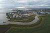 Luftaufnahme eines Industriehafens mit Tanks, Wasserwegen und grünen Feldern unter bewölktem Himmel.