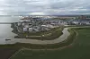 Luftaufnahme eines Industriehafens mit Tanks, Wasserwegen und grünen Feldern unter bewölktem Himmel.