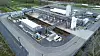 Luftbild einer Industrieanlage mit Tanks, Rohrleitungen und mehreren Gebäuden entlang einer Straße.