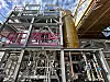 Stahlgerüst mit Rohrleitungen und großem zylindrischem Behälter in einer Industrieanlage.