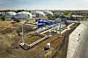 Industrieanlage mit weißen Lagertanks, Rohrleitungen und technischen Anlagen auf trockenem Gelände.