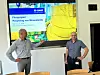 Zwei Männer vor einer Präsentation mit dem Titel „Pilotprojekt Recycling von Mineralwolle“ in einem Konferenzraum.