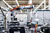 Industrieroboter in einer modernen Fabrikhalle mit Förderband und Monitoren.